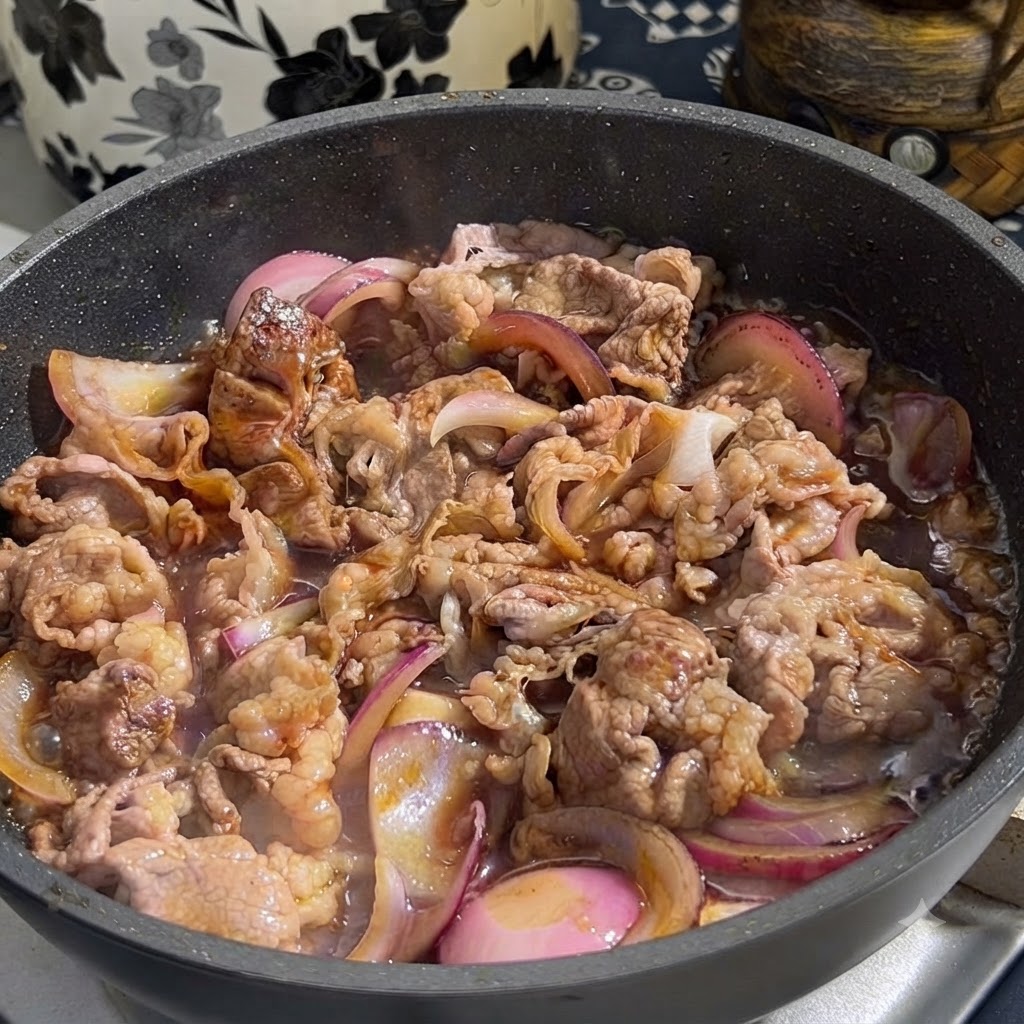 Teriyaki sauce being poured from a container into a frying pan containing browned beef and sliced red onions.