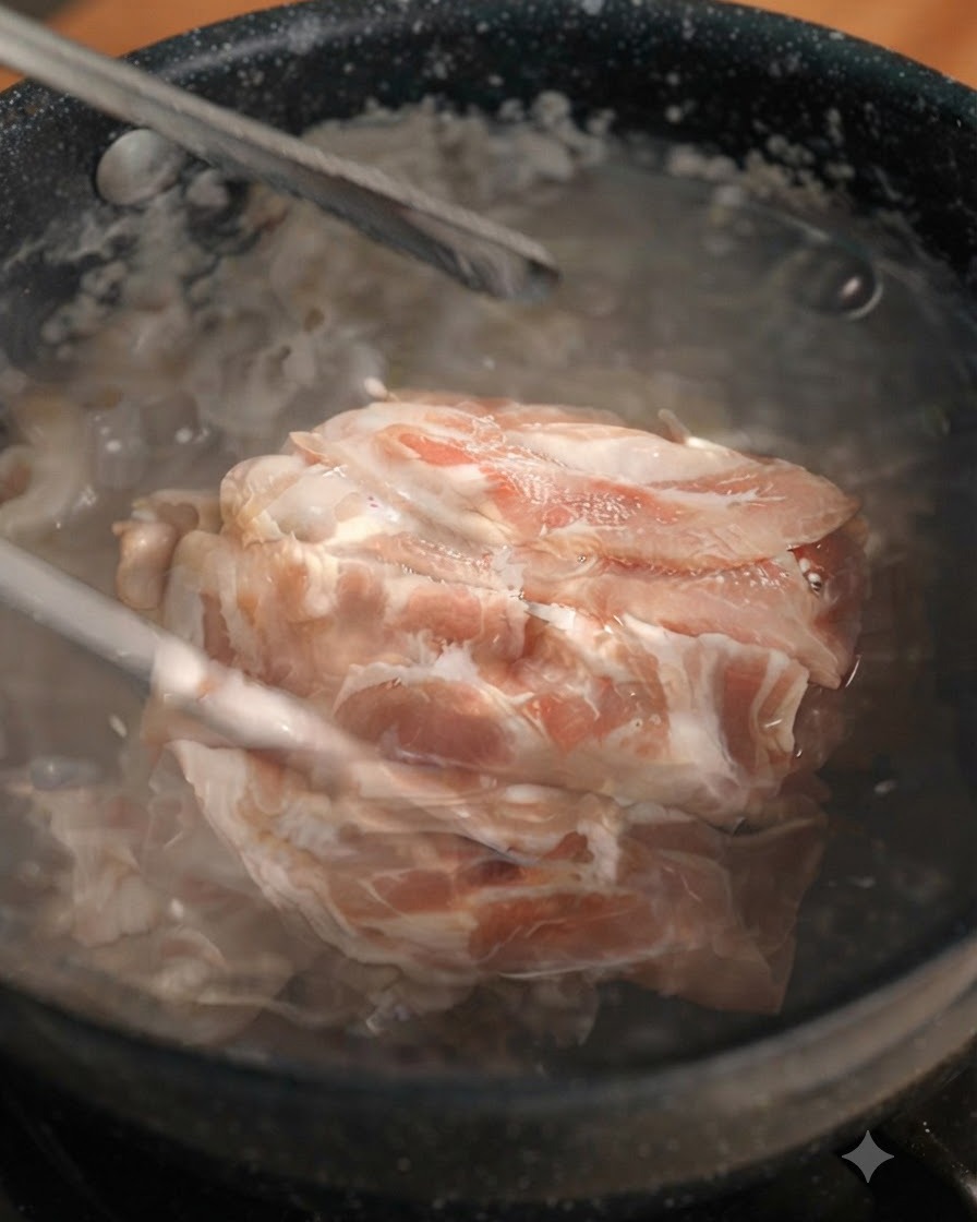 Blanched beef slices being lifted out of a boiling pot using tongs.