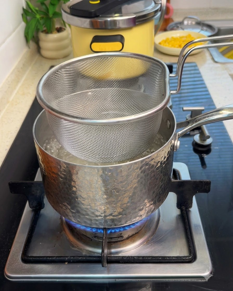 A mesh strainer basket submerged in a pot of boiling water on a stove with sliced beef.