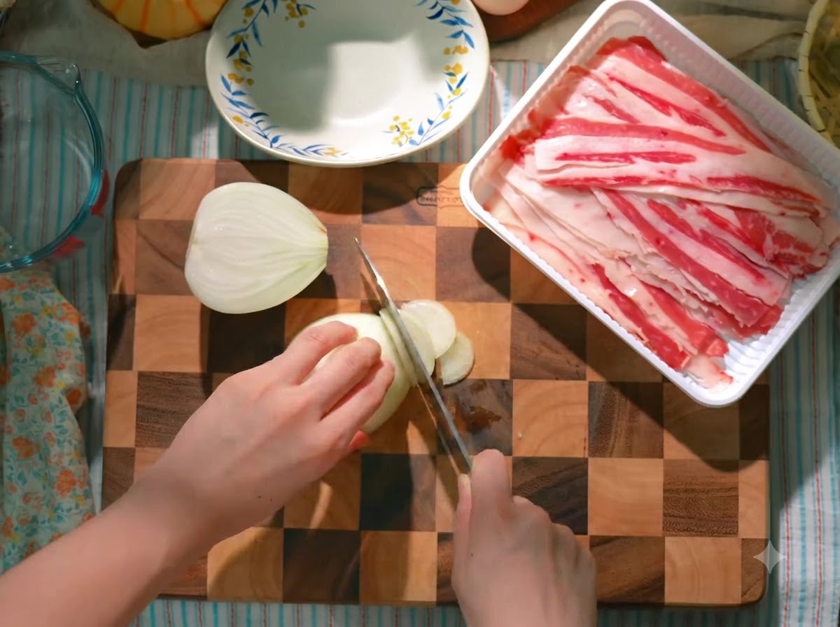 An onion being carefully sliced on a wooden cutting board beside a packaged tray of raw beef slices.