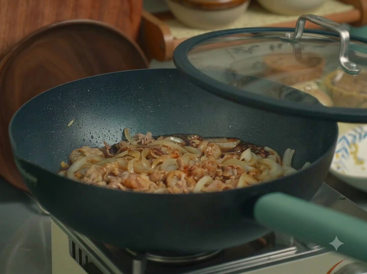 A pan filled with beef and onions covered with a glass lid on a stove.