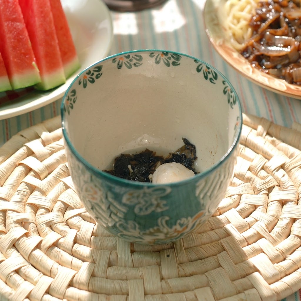 A cooked pork meatball and seaweed inside a patterned ceramic soup bowl.