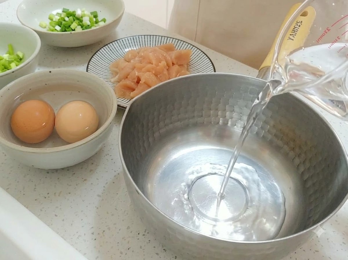 Clear water being poured from a measuring cup into a stainless steel pot.