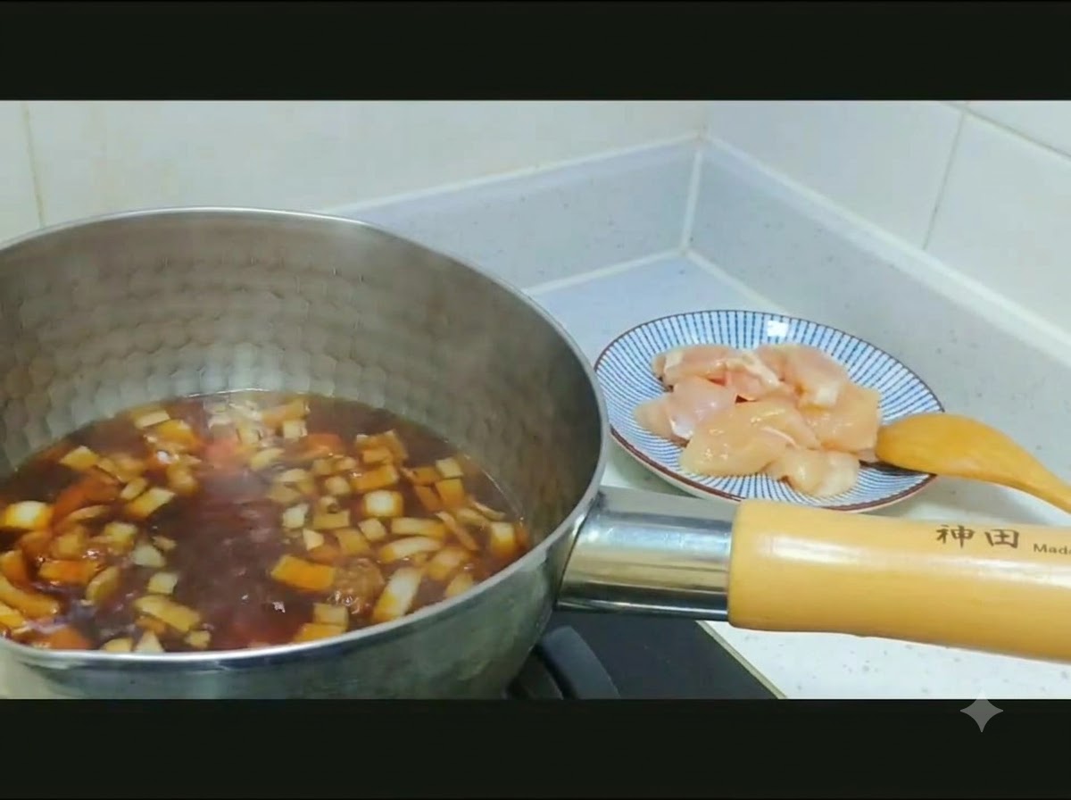 Raw diced chicken and sliced onions being transferred from a patterned plate into a pot of dark broth.