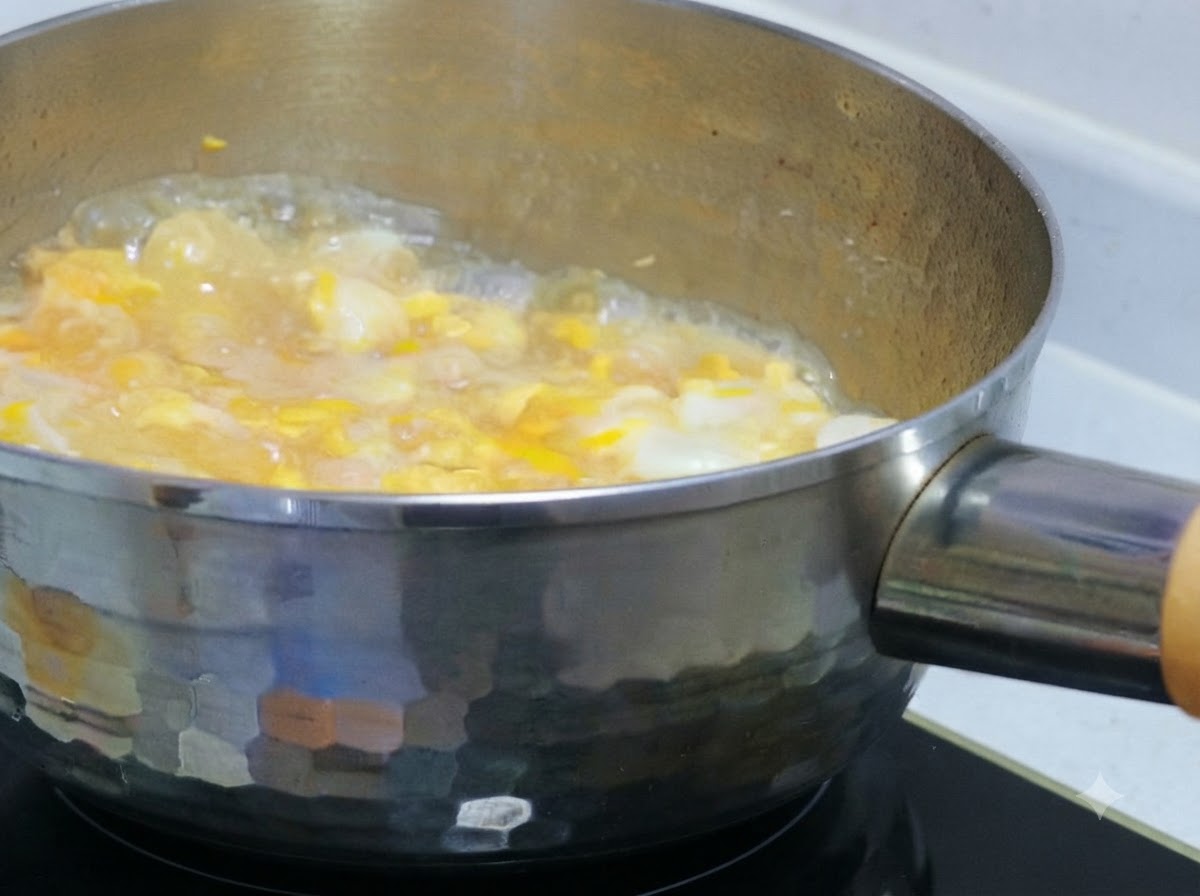 Partially beaten egg liquid being poured over simmering chicken and onions in a pot.