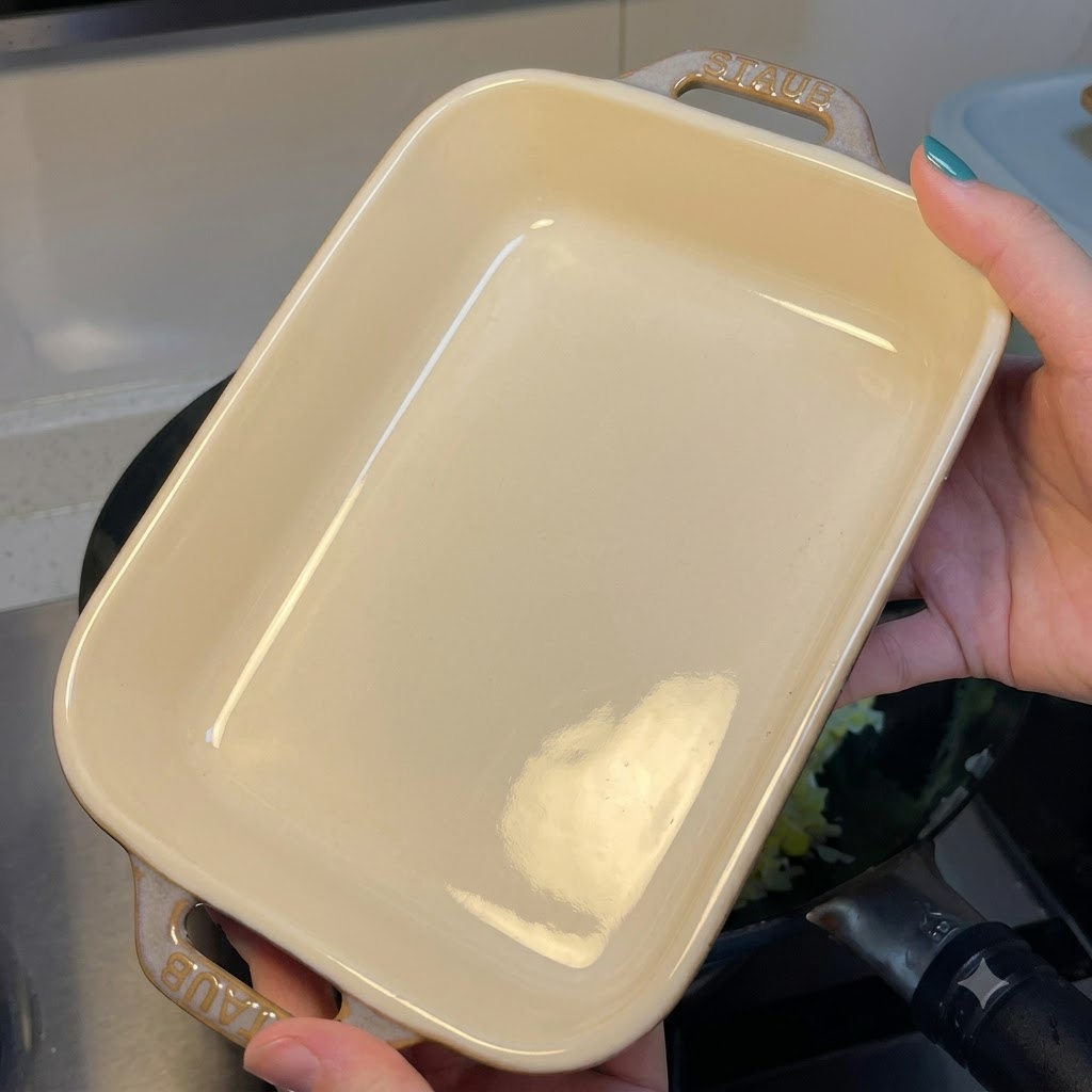 A person holding an empty rectangular white ceramic baking dish over a wok containing egg fried rice.