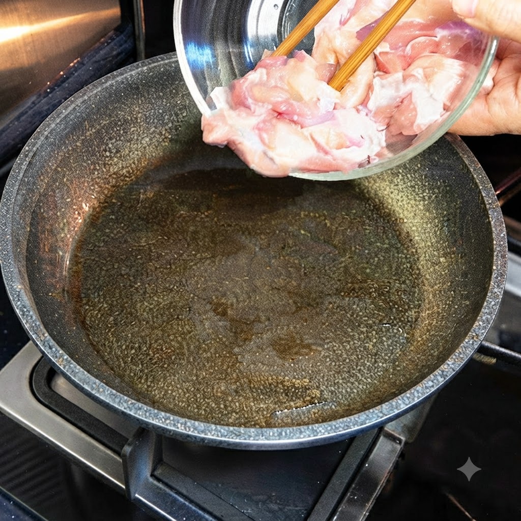 Raw chicken pieces being tipped from a glass bowl into a hot, oiled skillet.