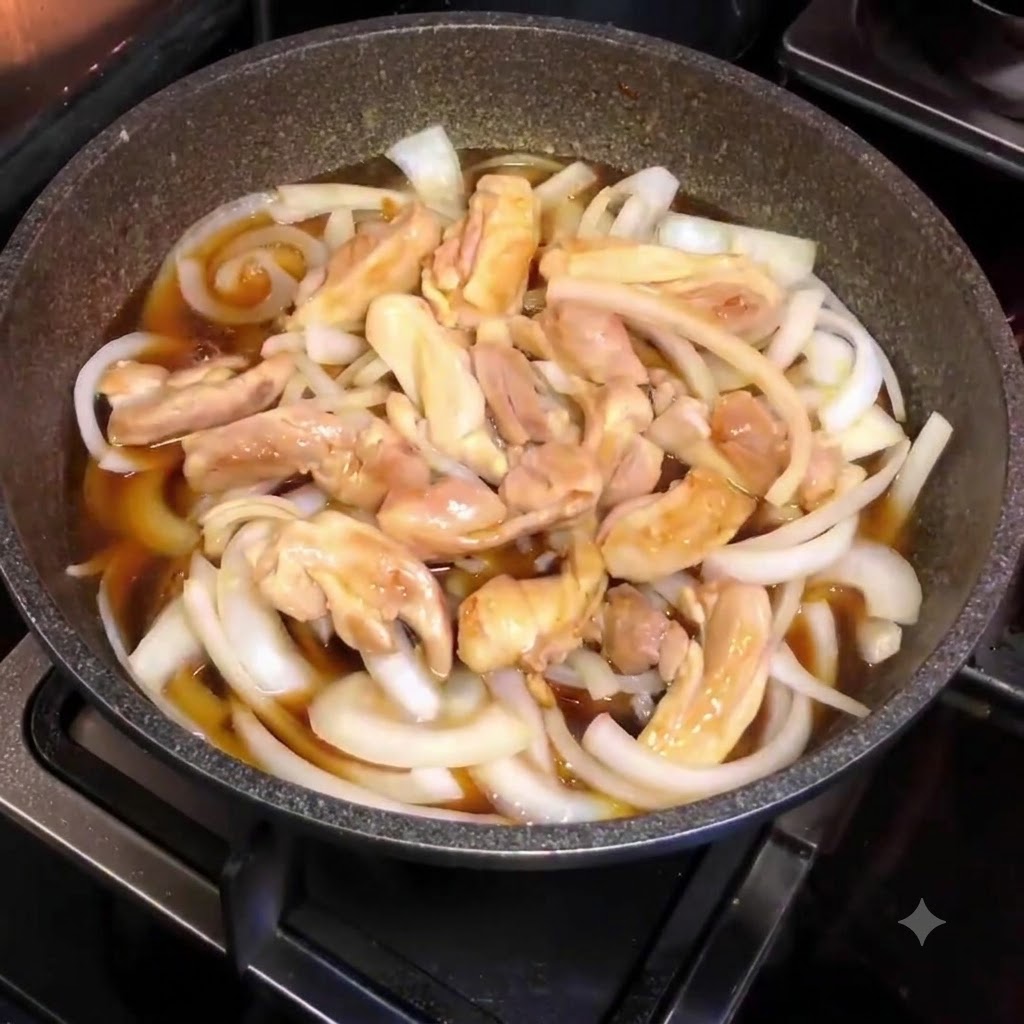 A pan filled with sliced onions, chicken pieces, and brown sauce, viewed from above during the simmering process.