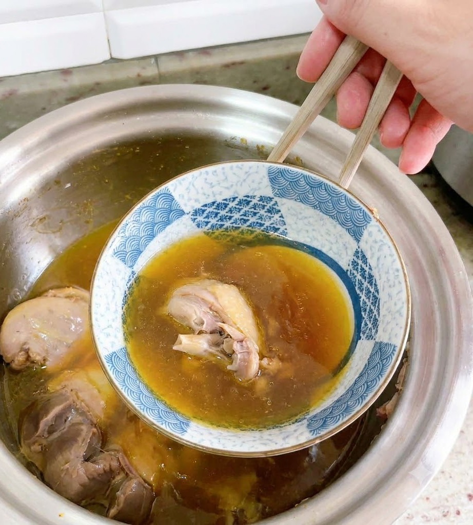 An inverted ceramic bowl is being carefully lifted out of the duck soup with chopsticks.
