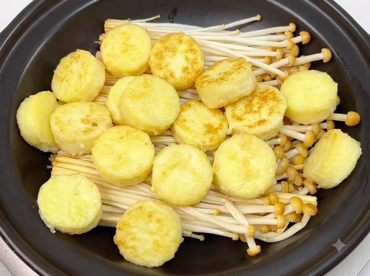 Golden pan-fried rounds of Japanese tofu neatly arranged on top of enoki mushrooms inside a black clay pot.