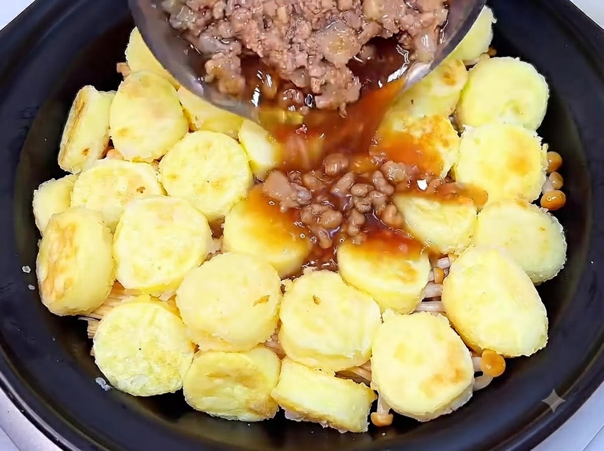 Cooked minced pork and dark savory sauce being poured from a pan over the layer of tofu inside the clay pot.