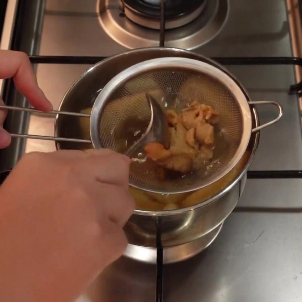 White miso paste being mixed inside a metal strainer submerged in a pot of hot soup using a spoon.