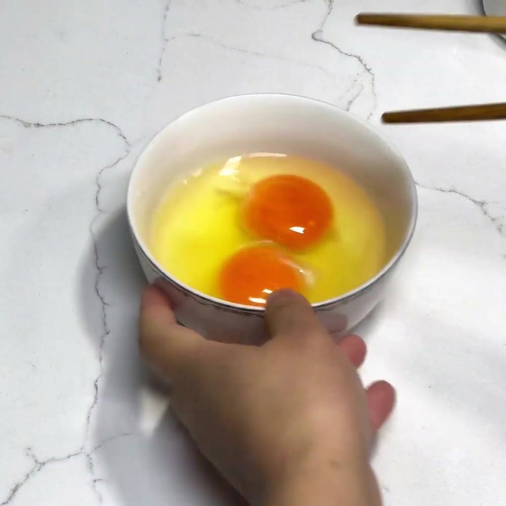 Two fresh eggs in a white bowl being beaten with wooden chopsticks without any seasonings.