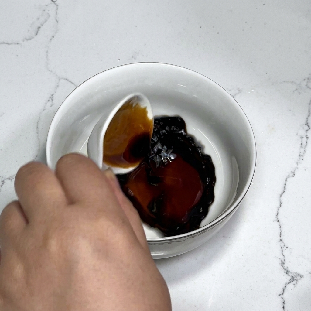 Sauce components including soy sauce, oyster sauce, sugar, and starch being stirred with water in a white bowl using a spoon.