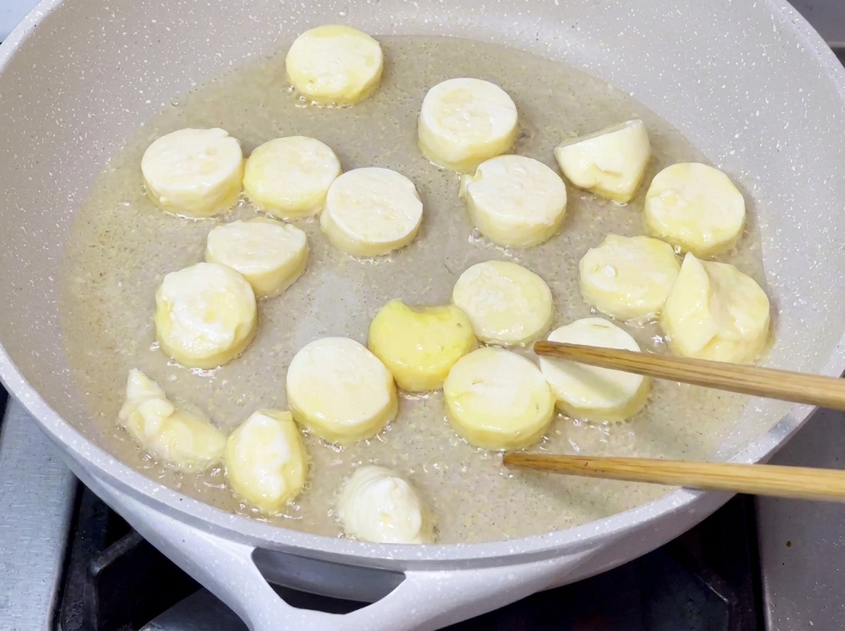 Tofu pieces frying in hot cooking oil in a pan until their surfaces turn golden and crispy.