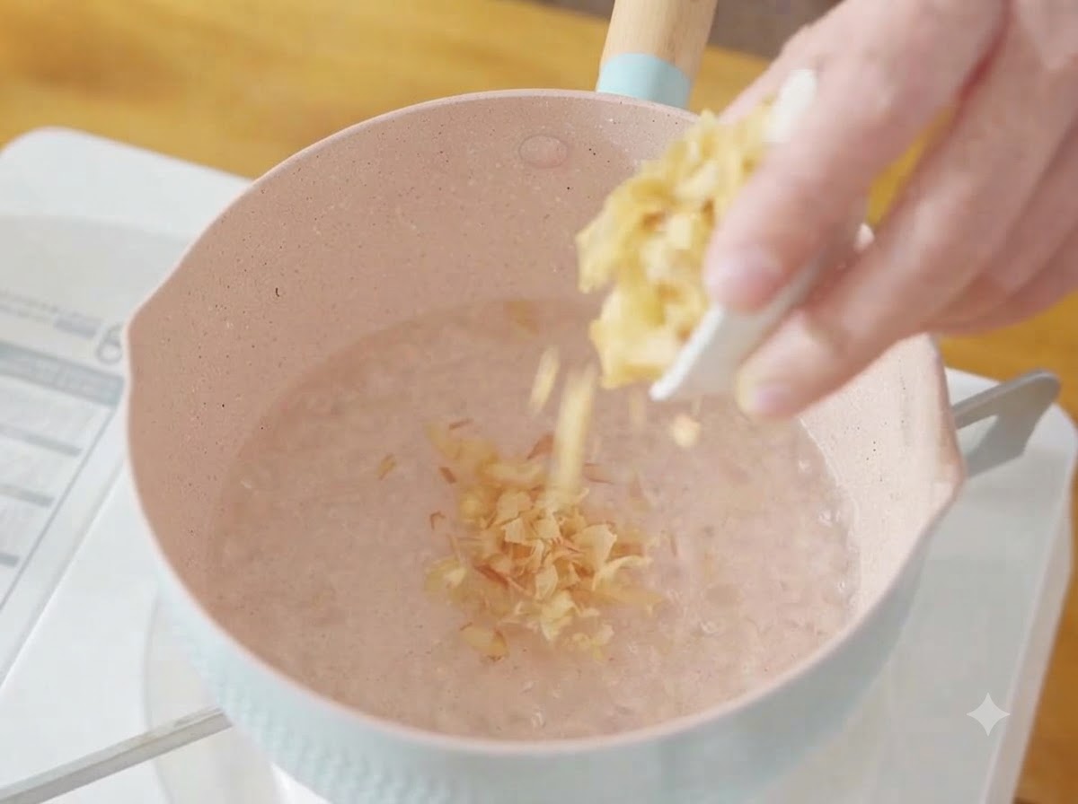 A handful of dry bonito flakes being dropped into a pot of boiling water.