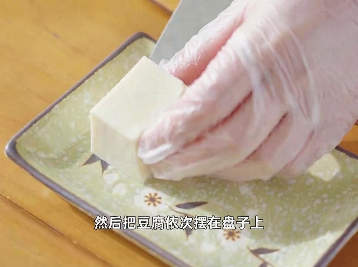 Gloved hands arranging a piece of cut silken tofu onto a decorative green plate.