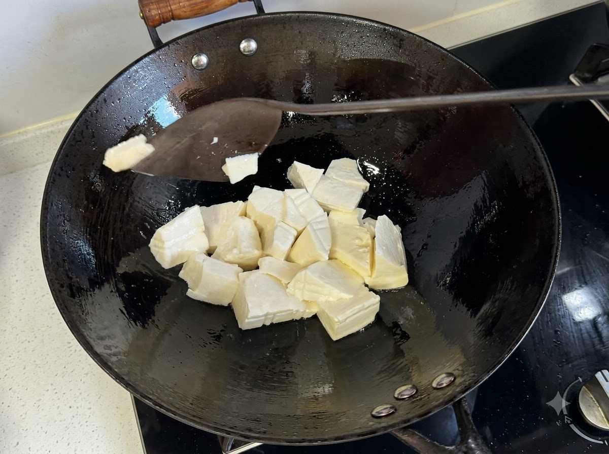 A spatula slicing through soft tofu pieces inside a hot frying wok.