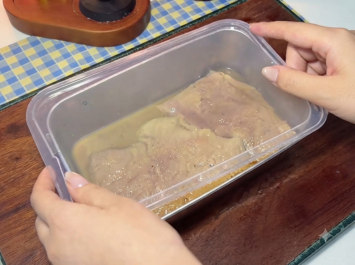 A plastic lid being placed onto a container filled with marinated pork cutlets and liquid.