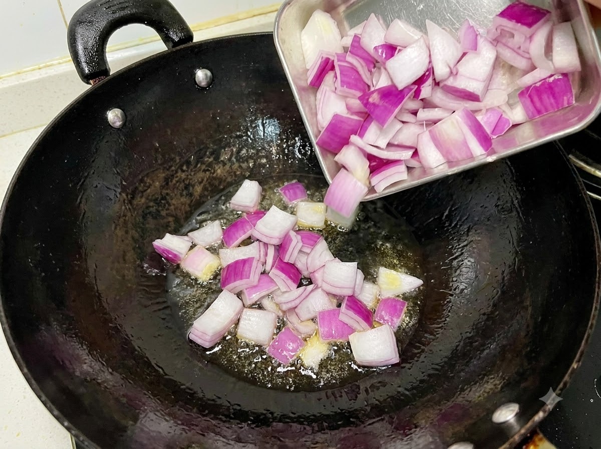 Diced red onions sizzling and being stir-fried in an oiled black wok.