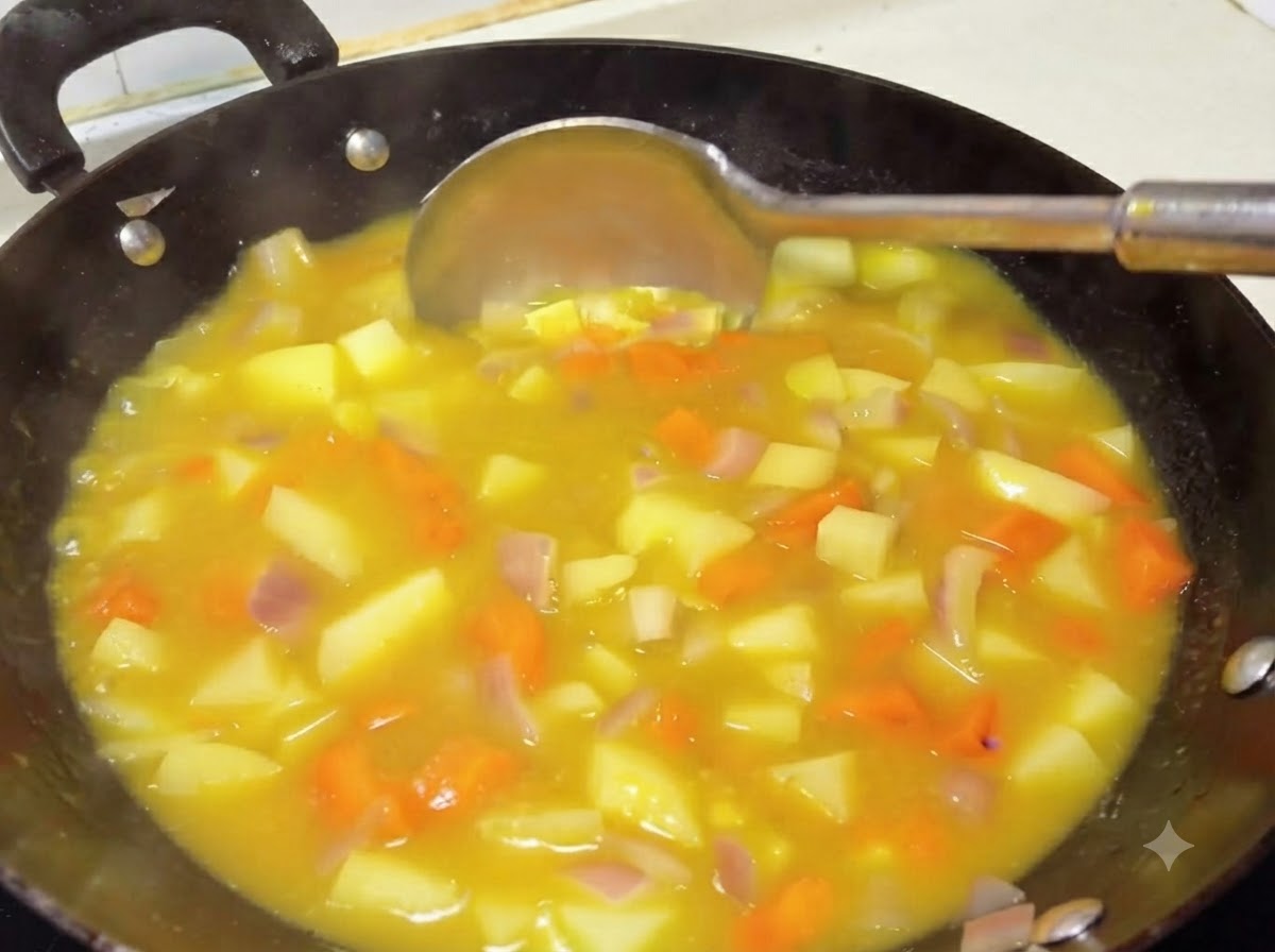 A ladle stirring a thick, rich yellow curry sauce with potatoes and carrots in a wok.