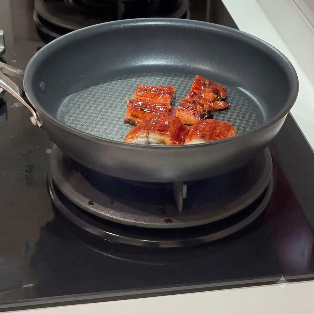 Several eel segments frying in a hot, dark non-stick pan on an induction cooktop.