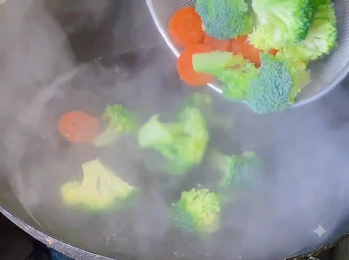 Broccoli florets and carrot slices being blanched in boiling water.