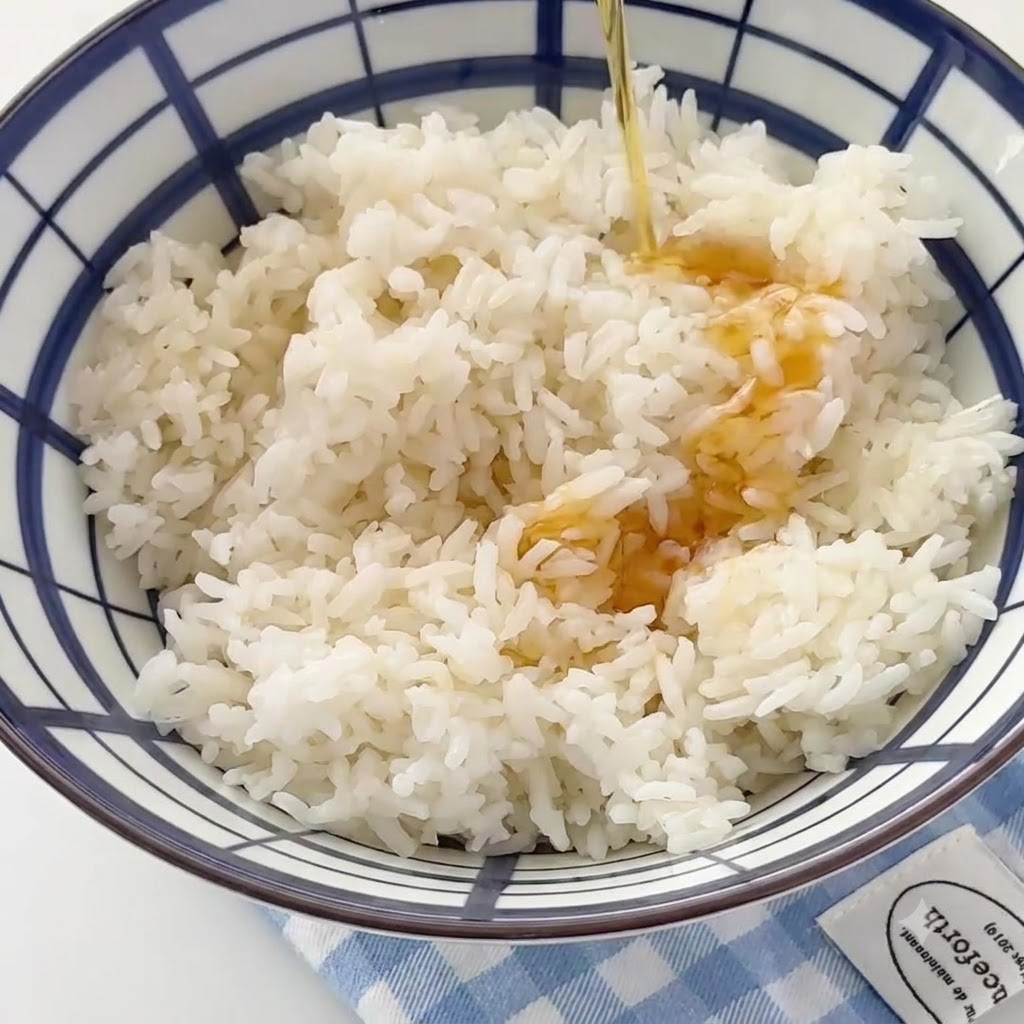 Sesame oil being streamed into a large bowl filled with white cooked rice.