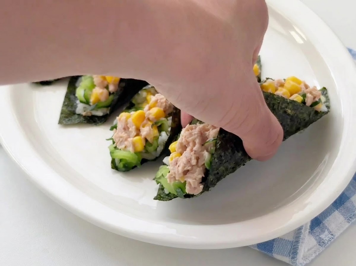 A hand placing or adjusting finished tuna seaweed rice rolls on a white serving plate.