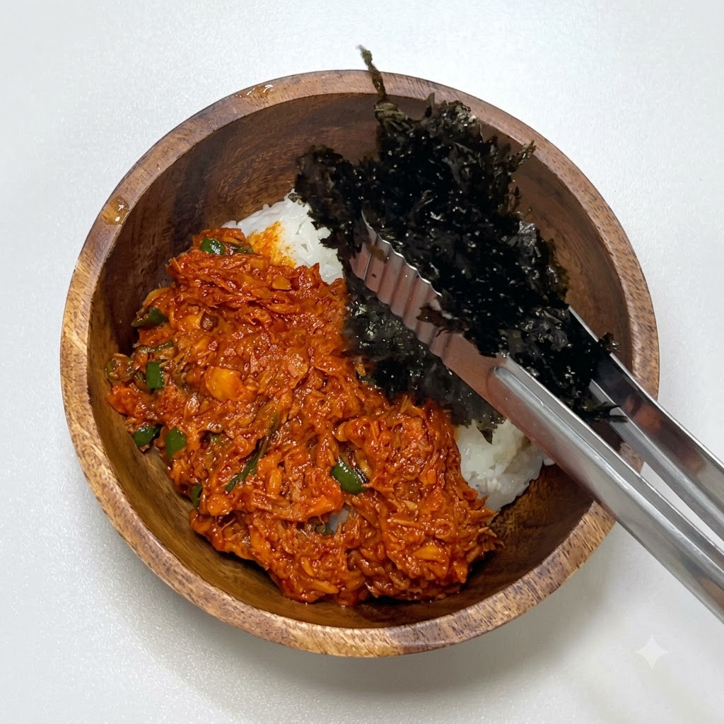 Metal tongs placing crushed dried seaweed into the wooden bowl next to the spicy tuna and rice.