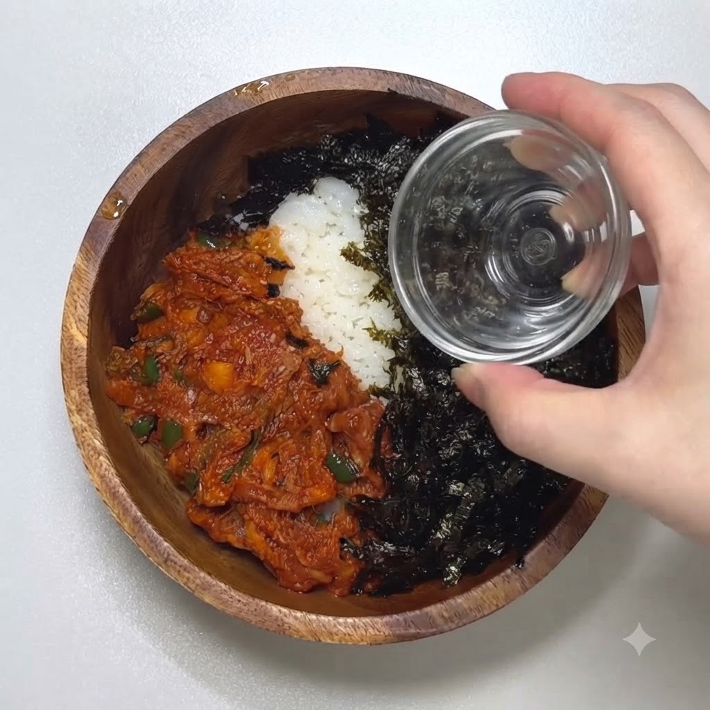 A close-up of a hand pouring toasted sesame seeds from a small glass container over a bowl filled with seasoned seaweed and spicy tuna.