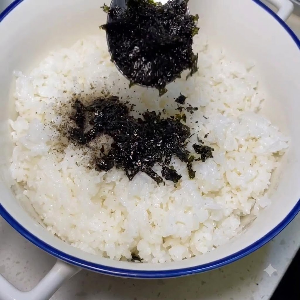 Seaweed powder being spooned and sprinkled over cooked white rice.