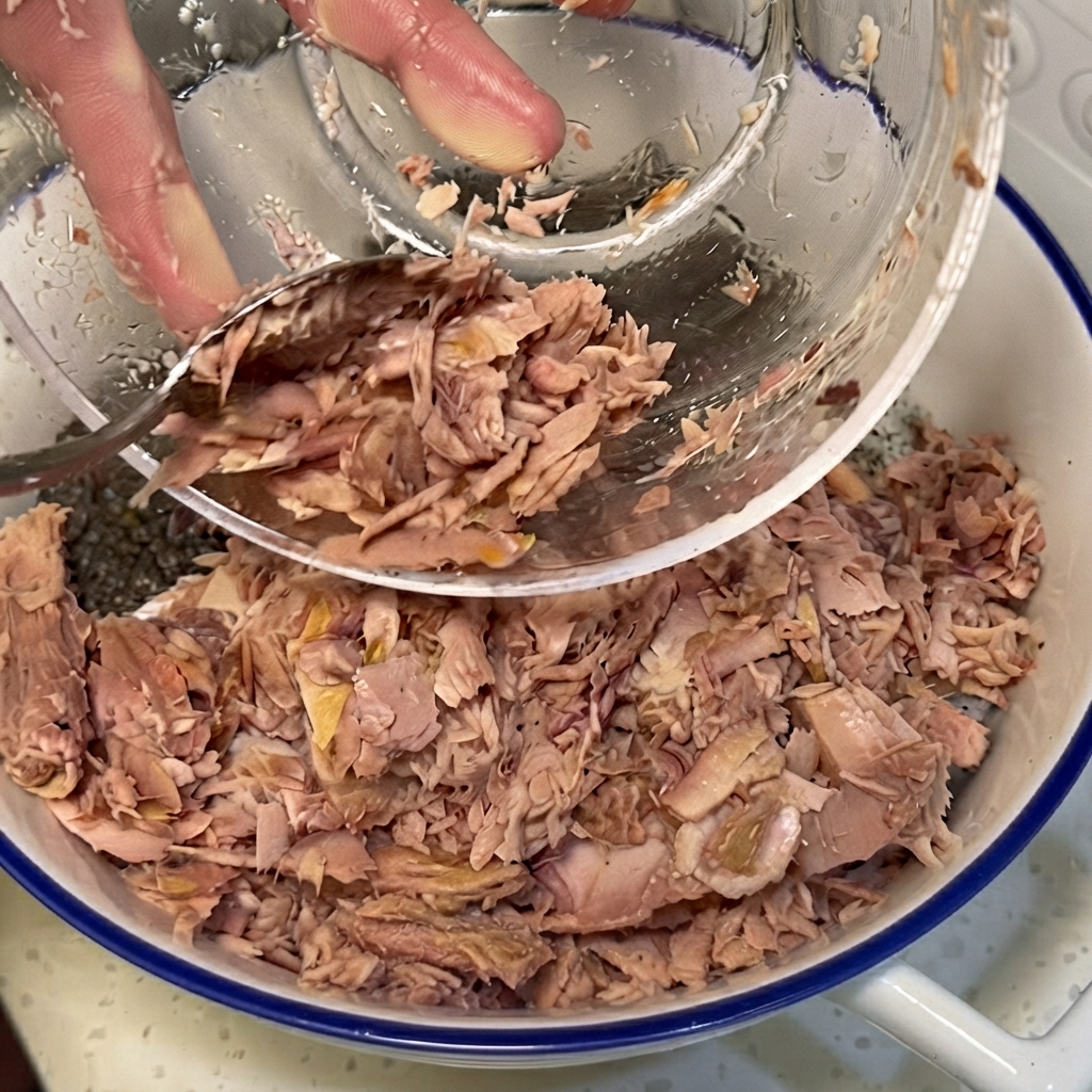 Shredded tuna, vegetables, and cabbage being arranged over seasoned rice in a large bowl.