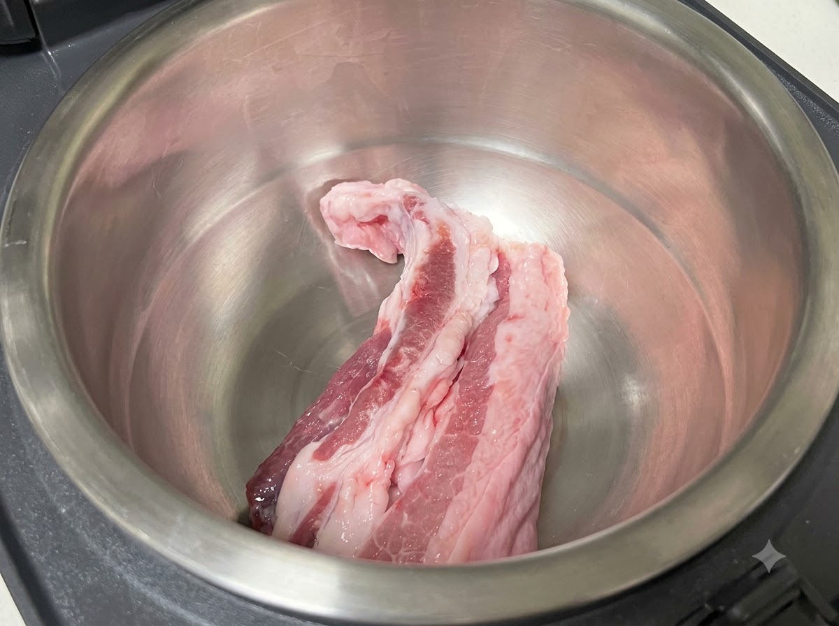 Raw pork belly strips resting inside the empty stainless steel inner pot of a rice cooker.