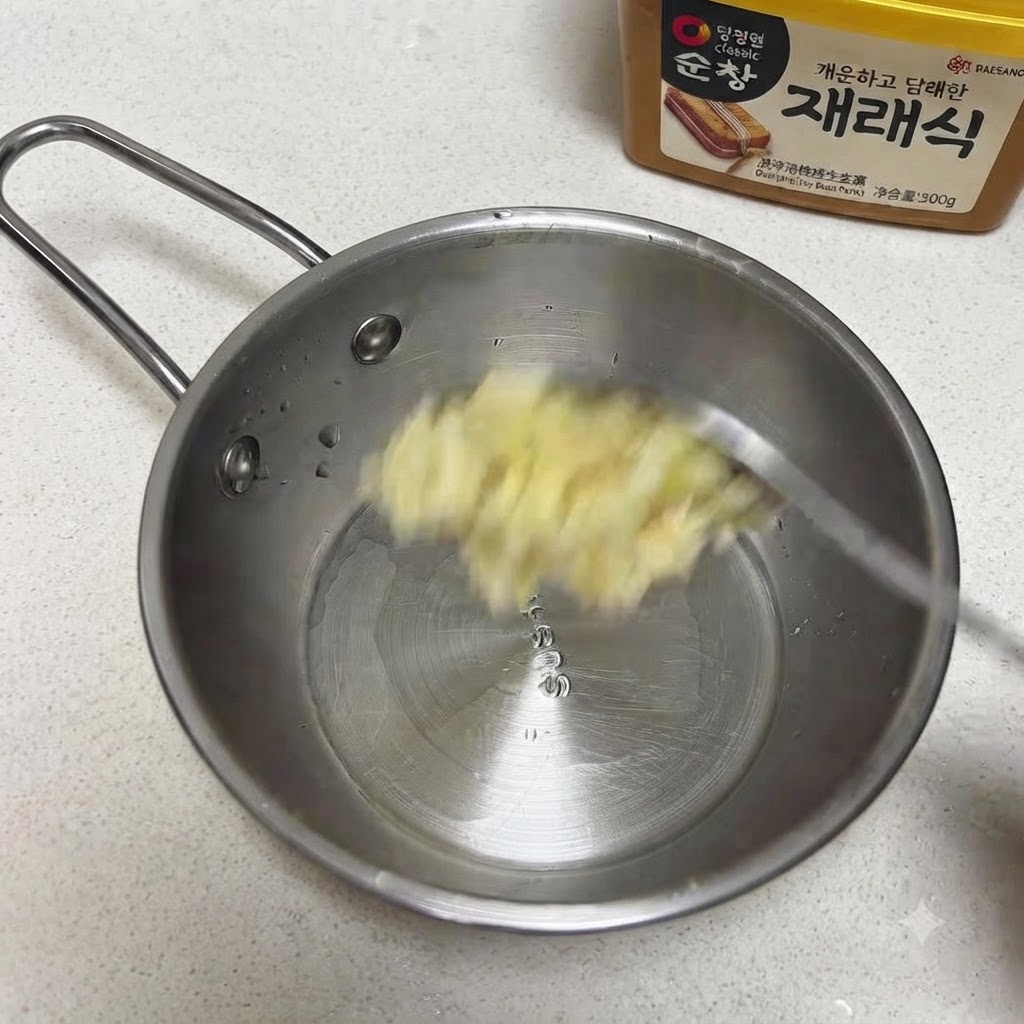 Minced garlic and sesame seeds being added to a small stainless steel pan.