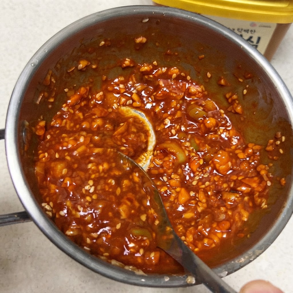 A spoon mixing a thick, vibrant red Korean dipping sauce inside a small metal pan.
