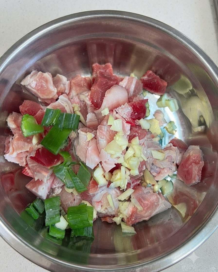 Raw pork belly cubes in a bowl combined with garlic, scallions, and red chili paste.