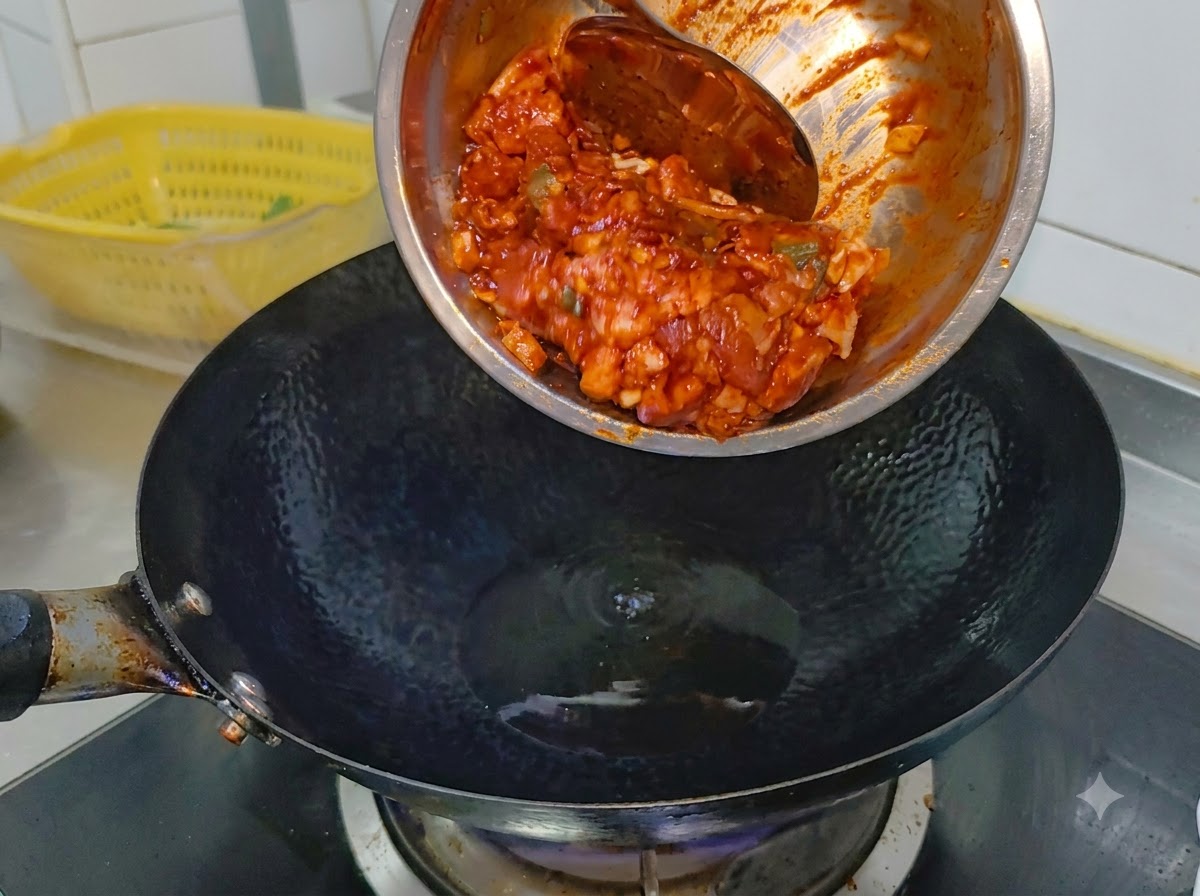 Marinated spicy pork belly sliding from a metal bowl into a smoking hot black wok containing cooking oil.