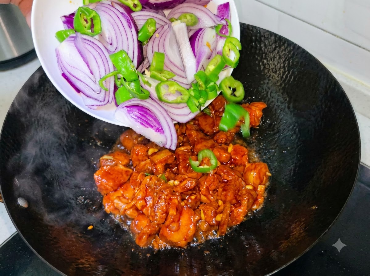 Slices of purple onion and green chili peppers being poured from a white plate into a wok with cooking pork belly.