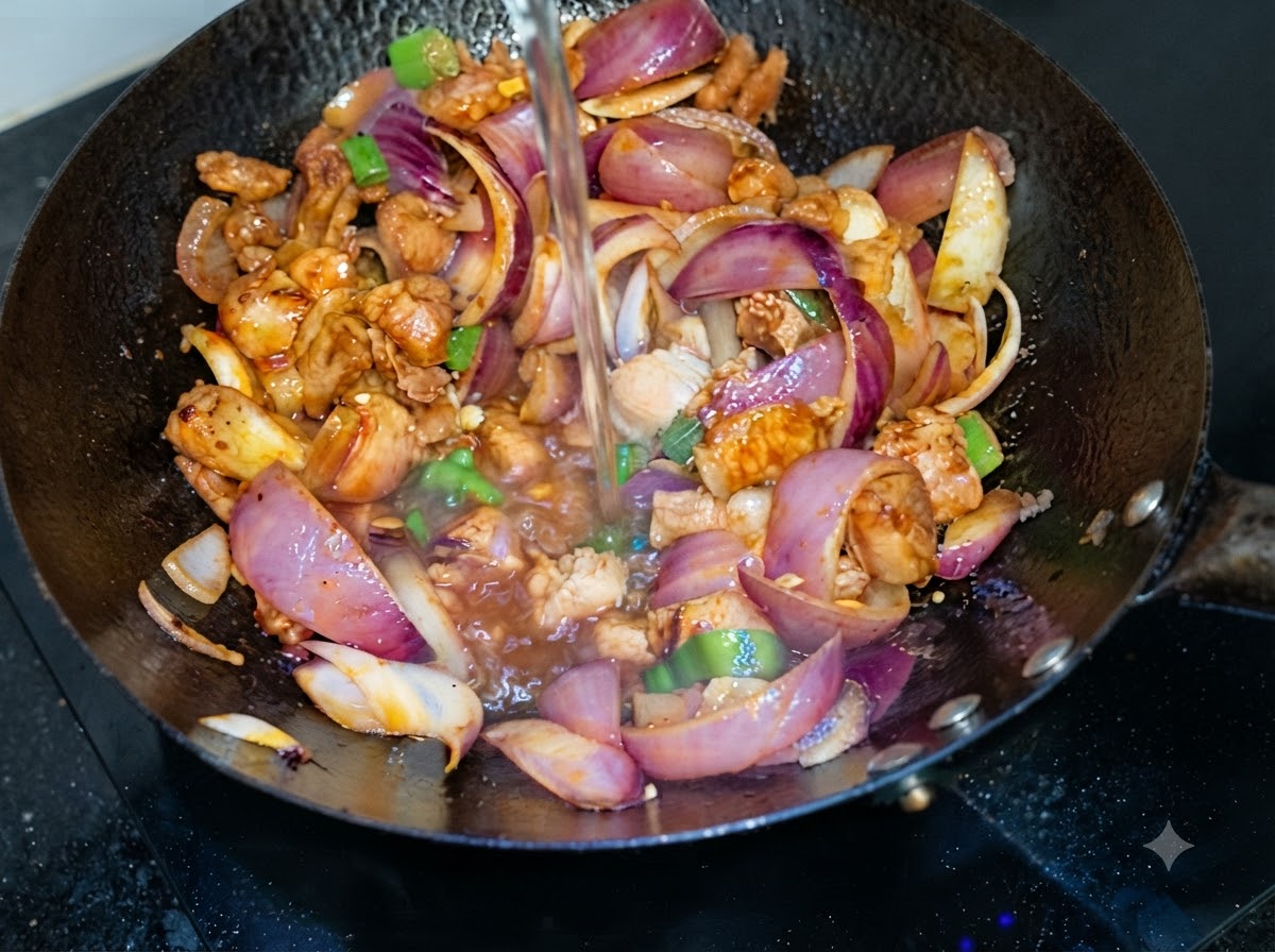 Water being poured from above into a wok containing stir-fried pork belly and purple onion slices.