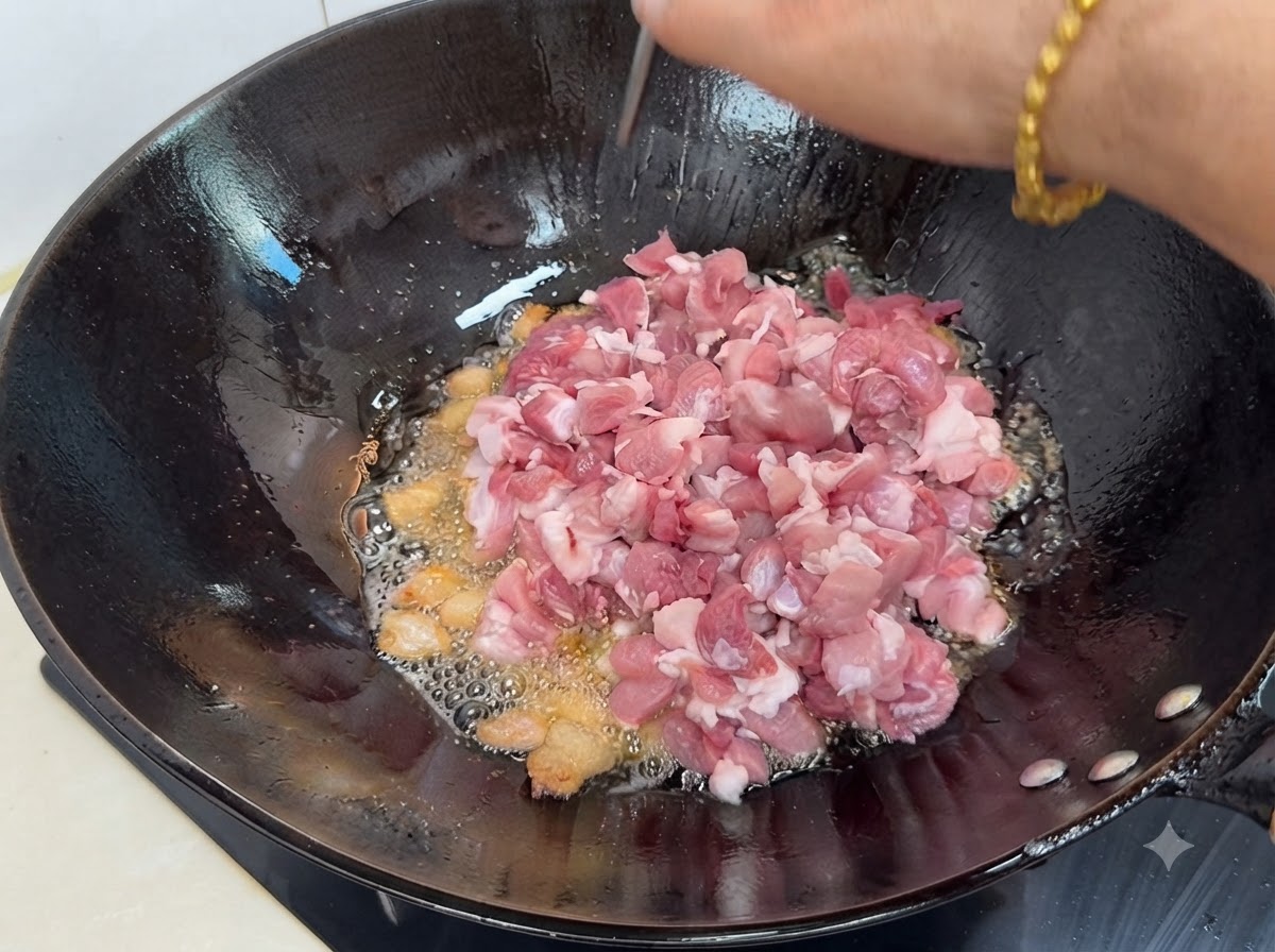Fresh diced lean pork pieces being added into the hot wok with rendered fat and spices.