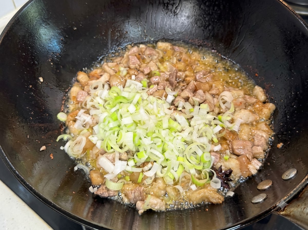 Chopped green scallions being stirred into the browned pork mixture in the wok.