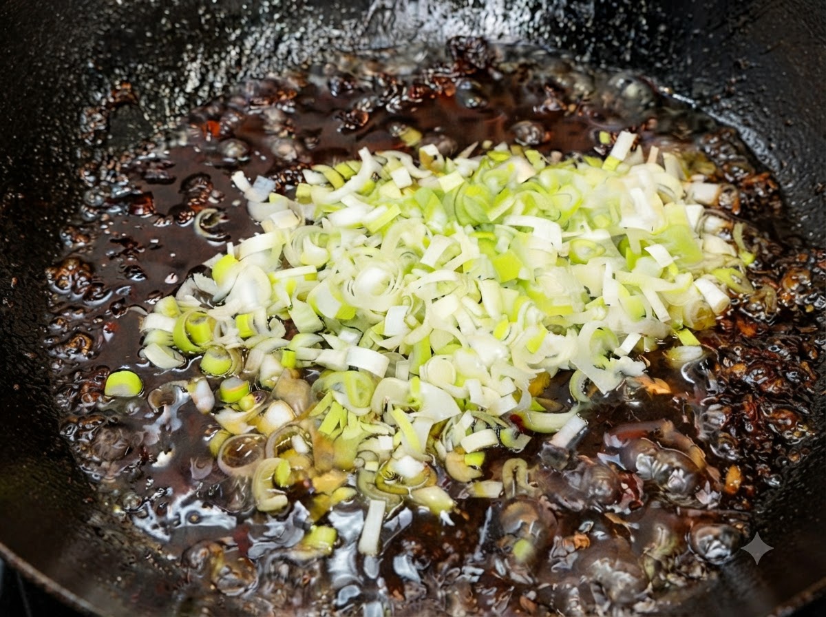 Freshly chopped green scallions being mixed into the hot finished fried sauce off the heat.