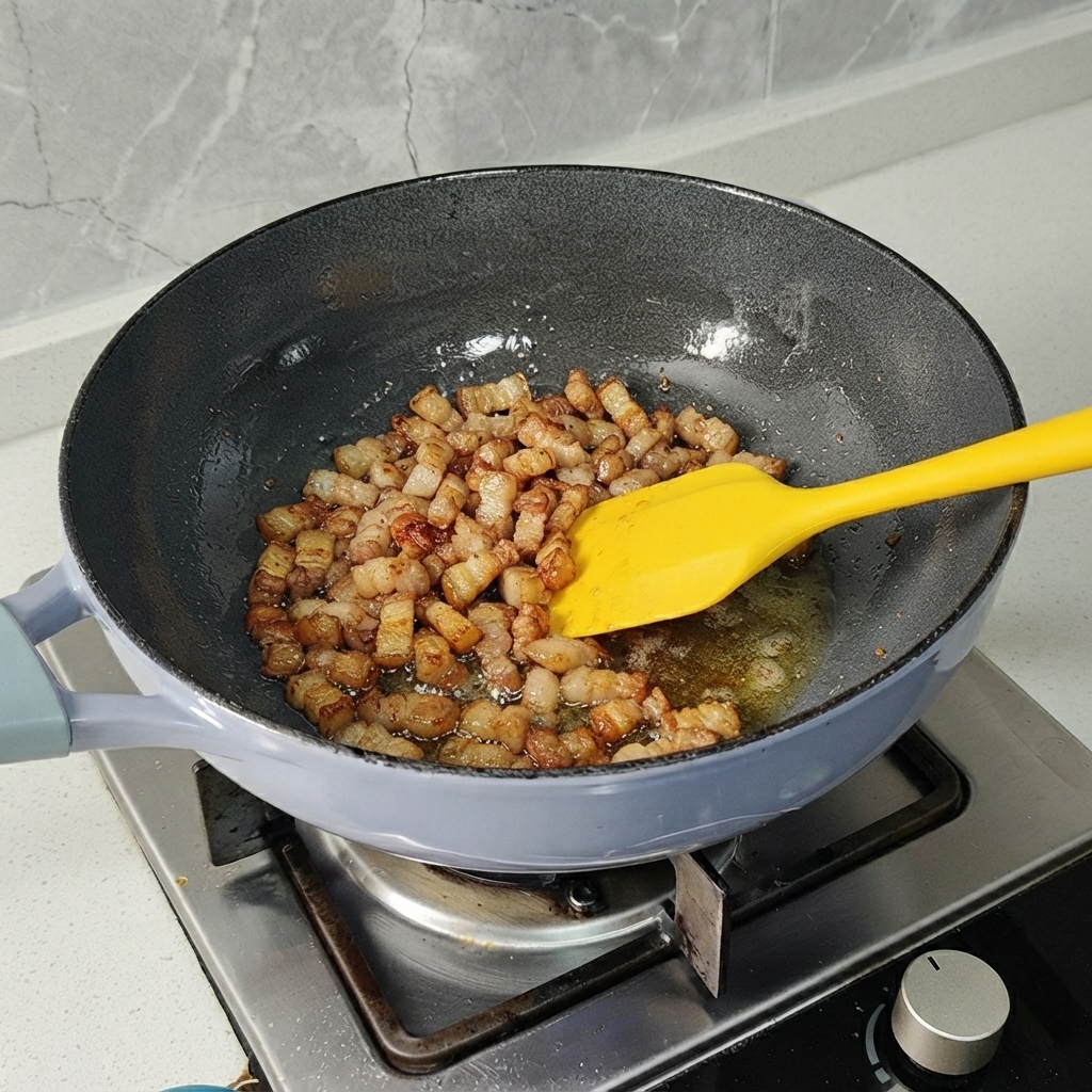 Pork belly pieces being stir-fried in a pan with a yellow spatula until lightly browned.