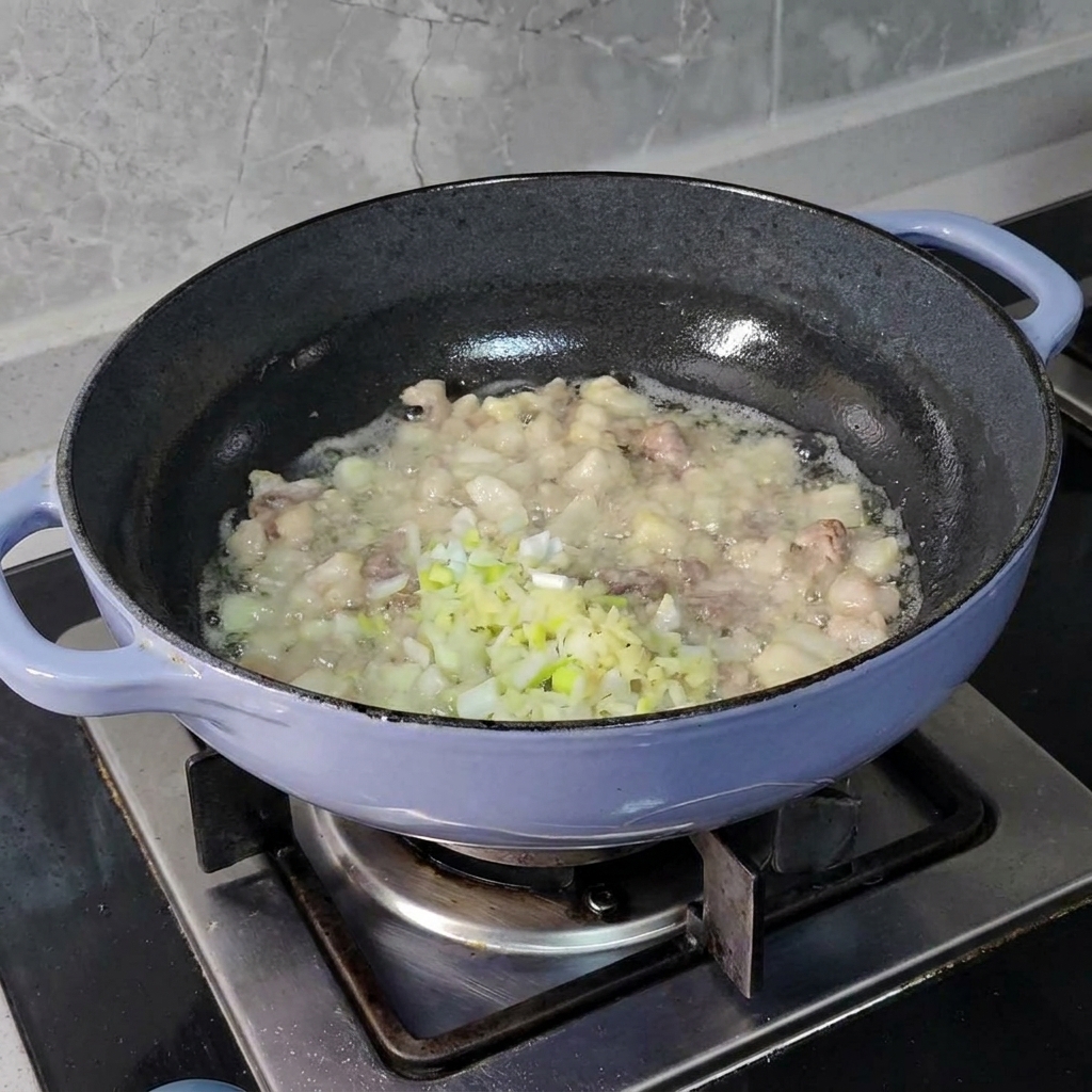 Finely chopped scallions, ginger, and garlic being added to sizzling pork pieces in a dark skillet.