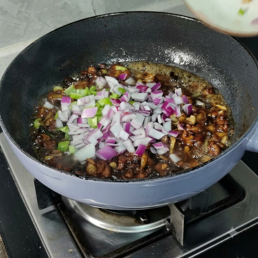 Diced red onions and green bell peppers scattered over a simmering dark sauce in a pan.