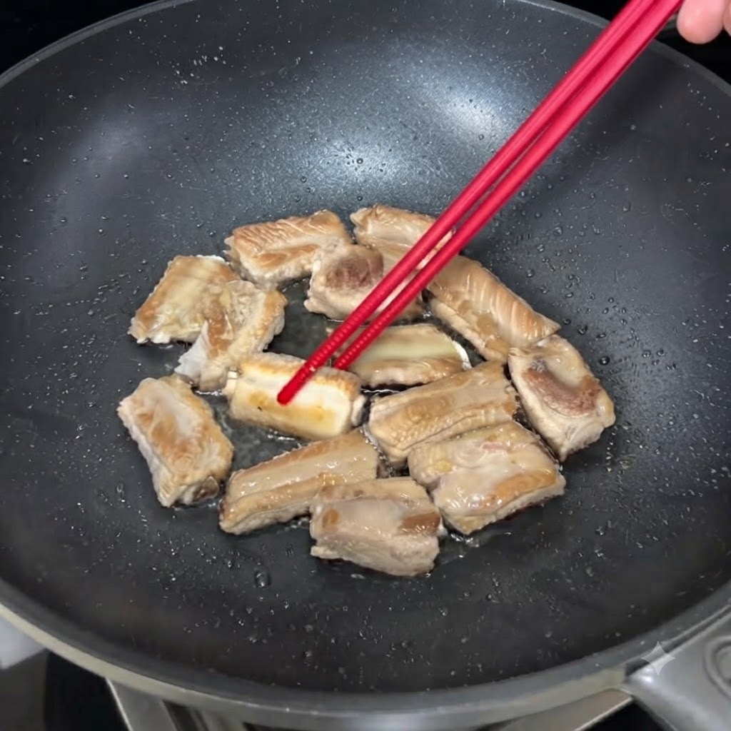 Pork ribs sizzling in a pan being turned over with chopsticks to brown evenly.