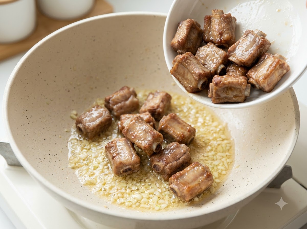 Pan-fried pork ribs being poured into a pan containing sautéed minced garlic and butter.
