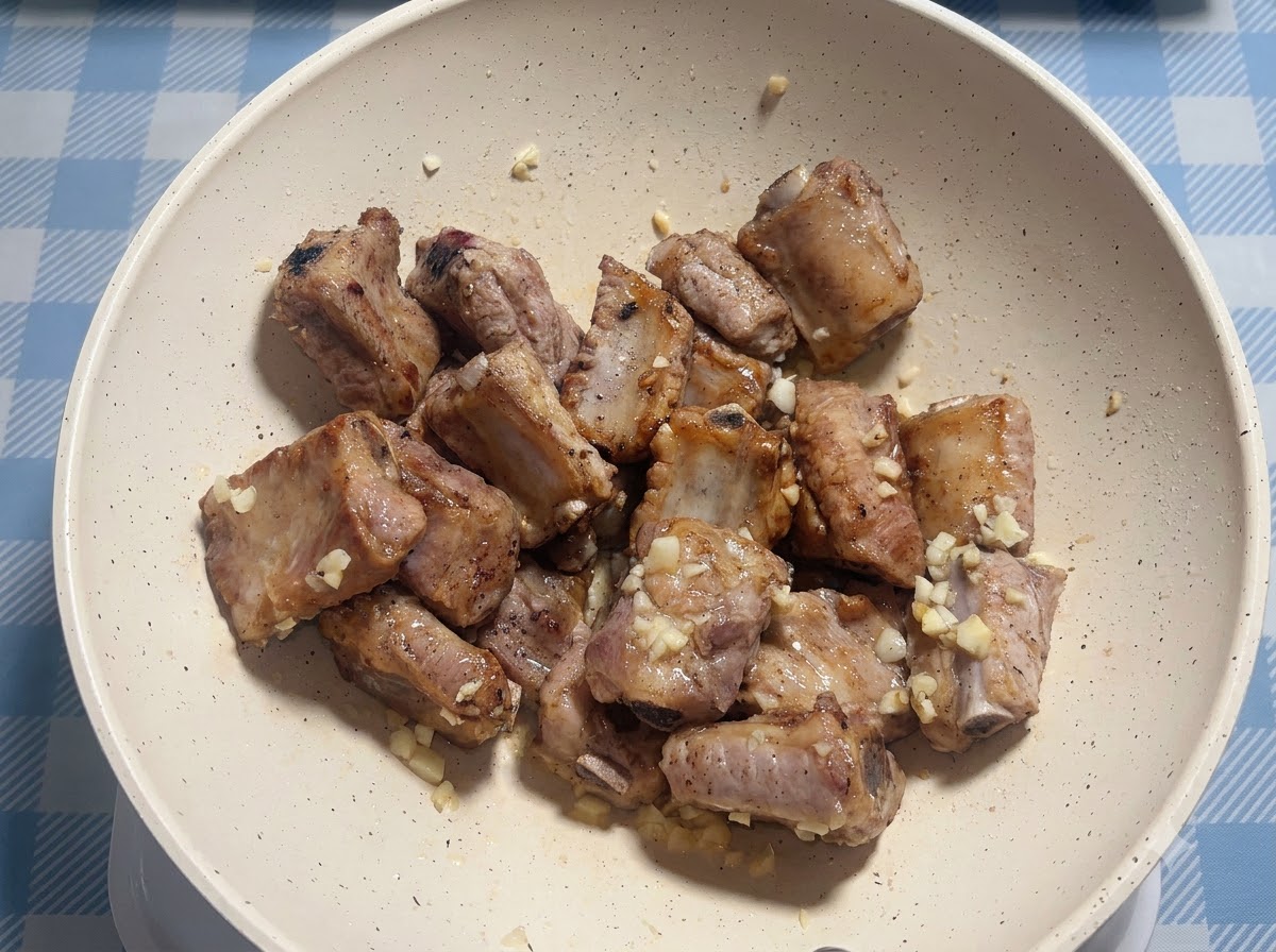 Pork ribs being seasoned with sauce inside a white frying pan.