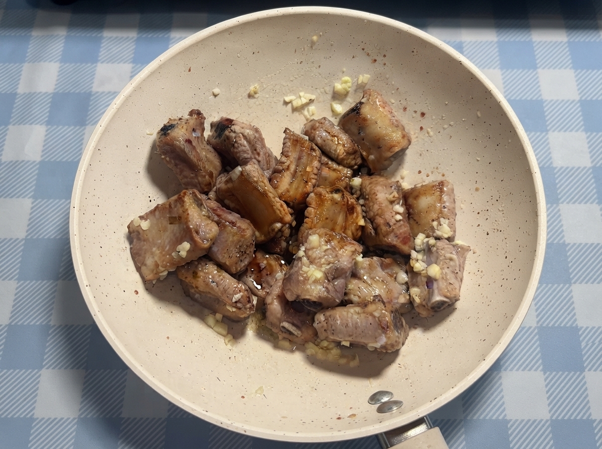 Pork ribs being drizzled with sauce and honey in a pan before final tossing.